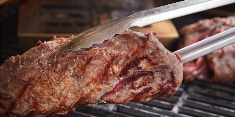 Fleisch mit der Grillzange auf dem Grill wenden